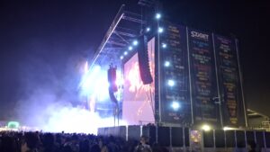 Vista nocturna de un gran escenario en el Sziget Festival. Focos y pantallas LED iluminan el escenario, mientras una gran multitud se reúne frente a él. En el lateral de la estructura del escenario cuelgan grandes pancartas con el logotipo de Sziget y los nombres de varios artistas.